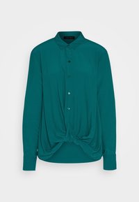 Chemise boutonnée teal avec col. Coupe ample, présente un design devant noué. Manches longues avec poignets à boutons et texture de tissu lisse.