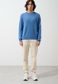 Blauer Strickpullover mit Rundhalsausschnitt, kombiniert mit beigen Hosen. Die Textur sieht weich aus, und die Passform ist entspannt. Weiße Sneaker runden das Outfit ab.