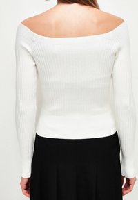 Weißes, schulterfreies, geripptes Strickoberteil mit langen Ärmeln, figurbetontem Design und Texturvariationen im Stoff, kombiniert mit einem schwarzen Rock.