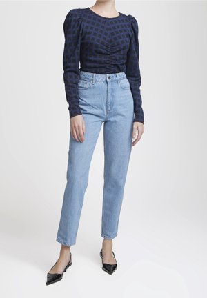 Kvinde iført lyseblå jeans med høj talje, navyblå langærmet top med ternet mønster og sorte slingback-sko med spids tå.