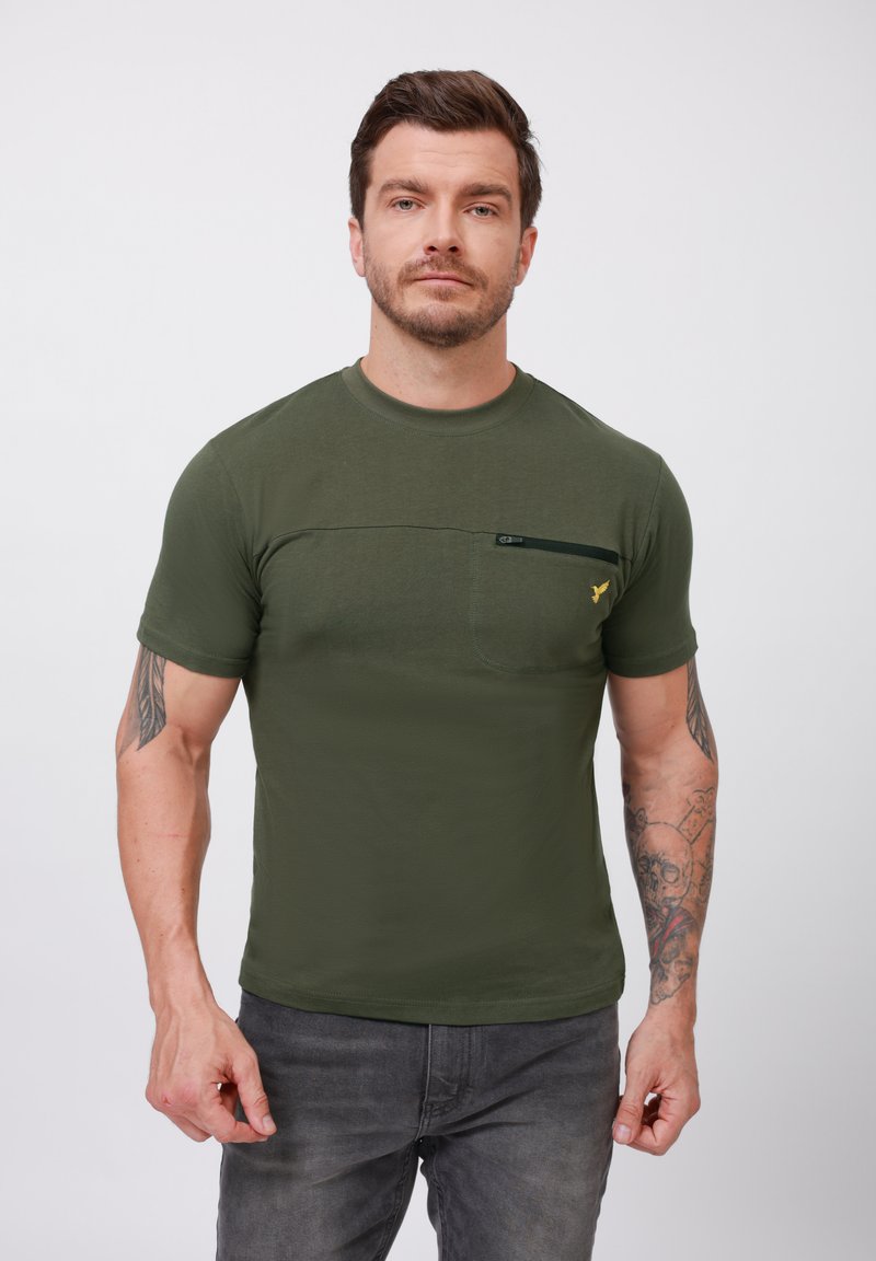 Olivengrøn kortærmet t-shirt med rund halsudskæring, prydet med en påsyet lomme og en kontrasterende lynlåsdetalje; stoffet virker glat og let.