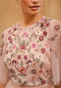  embroidered blush ylin featuring floral designs in pink, purple, and gold tones, with sheer sleeves and sequin accents for added texture.