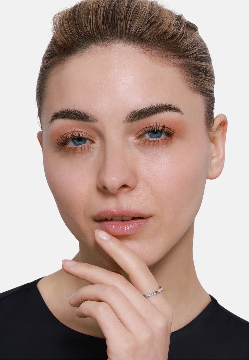 Srebrny pierścionek z gładkimi, zaokrąglonymi kamieniami. Modelka ma jasną cerę, niebieskie oczy i neutralny makijaż, a także minimalistyczny czarny top. Palec dotyka brody.