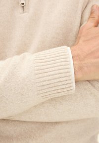 Beige gebreide sweater met een kwart-rits kraag, geribde manchetten en een zachte textuur met een subtiel patroon.