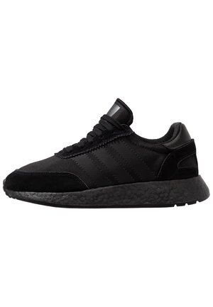 Baskets basses noires avec dessus en mesh et suède, semelle en mousse texturée, trois bandes cousues sur le côté et lacets noirs.