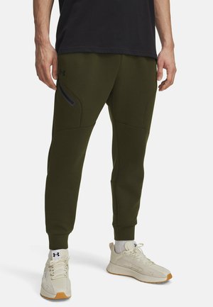 Gröna joggingsbyxor med smal passform, elastisk midja, fickor med dragkedja och textilstruktur. Kombinerade med krämfärgade sneakers för kontrast.