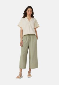 Haut crème à manches courtes avec un col, associé à un pantalon large vert clair et des sandales blanches à lanières, avec une coupe décontractée et une taille à cordon.
