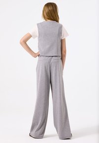 Grijze gestructureerde jumpsuit met wijde broekspijpen en een cropped top, voorzien van verticale strepen en minimalistische ontwerpelementen.