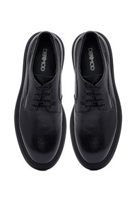 Zwarte leren dresschoenen met een gestructureerde afwerking, voorzien van een ronde neus, een minimalistisch vetersysteem en een stevige rubberen zool.