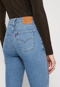 Jeans en denim bleu clair avec une coupe ajustée, dotés d'une écusson en cuir à l'arrière et de deux poches arrière avec des coutures contrastantes.