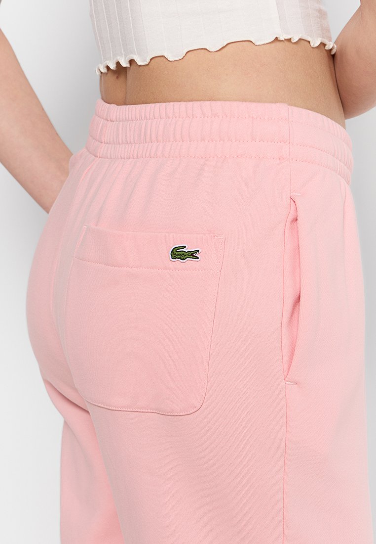 Roze joggingbroek van zacht materiaal, met een ribgebreide tailleband en een achterzak met een klein groen krokodillenlogo.