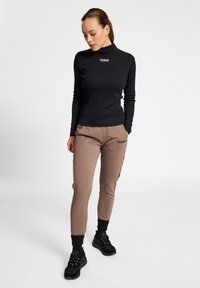 Zwarte lange mouwen top met een mock neck en klein logo; beige aansluitende broek met zijzak en zwarte details; zwarte sneakers met een gestructureerde zool.