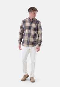Kariertes Hemd in Beige, Marineblau und Braun mit langen Ärmeln und Knopfverschluss. Kombiniert mit cremefarbenen Hosen und braunen Stiefeletten. Glatte Textur.