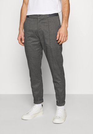 Grau gemusterte Hose mit schlanker Passform, ausgestattet mit aufgerolltem Saum, glatter Textur und einem dunklen Bund, kombiniert mit weißen Sneakers.