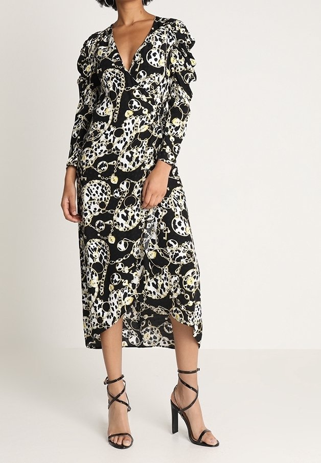 Robe noire avec un décolleté en V, des manches longues et des détails froncés. Présente un motif de crâne et de chaîne en blanc et jaune. Longueur mi-mollet, tissu fluide.