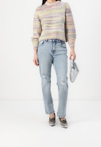 Kolorowy dzianinowy sweter z okrągłym dekoltem, zestawiony z jasnymi, przetartymi jeansami i srebrną torebką z węzłem.