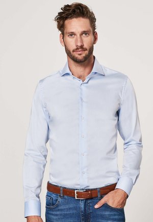 Light blue long-sleeved shirt made of smooth fabric, featuring a button-down front and a collar. Worn with a brown belt and blue jeans.