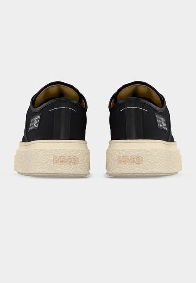 Ζευγάρι μαύρα χαμηλά αθλητικά παπούτσια με χοντρές υφασμάτινες μπεζ σόλες, ορατή ραφή και ένα μικρό ορθογώνιο ταμπελάκι στο πλάι.