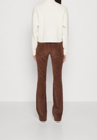 Pantalon évasé en velours côtelé marron avec poches arrière, associé à un pull court texturé crème. Vue montrant l'arrière de la tenue.