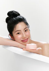 Contenant crème rose étiqueté "Abib PORN patch rétinien pour les yeux", tenu dans une main. Forme lisse et arrondie avec un couvercle transparent. Fond clair.