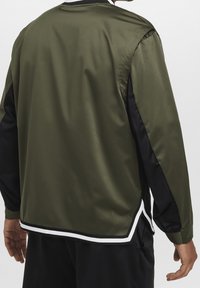 Oliwkowo-zielona kurtka z czarnymi rękawami i białymi akcentami. Charakteryzuje się gładką, błyszczącą fakturą, prążkowanym kołnierzem oraz bocznymi rozcięciami. Luźny krój.