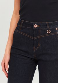 Dark blue denim jeans featuring copper accents, orange stitching, and classic five-pocket design. Button closure at the waist.