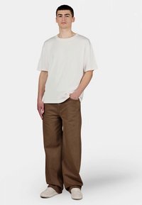 White short-sleeve t-shirt paired with brown wide-leg pants and white sneakers. The t-shirt has a relaxed fit, and the pants are smooth-textured.