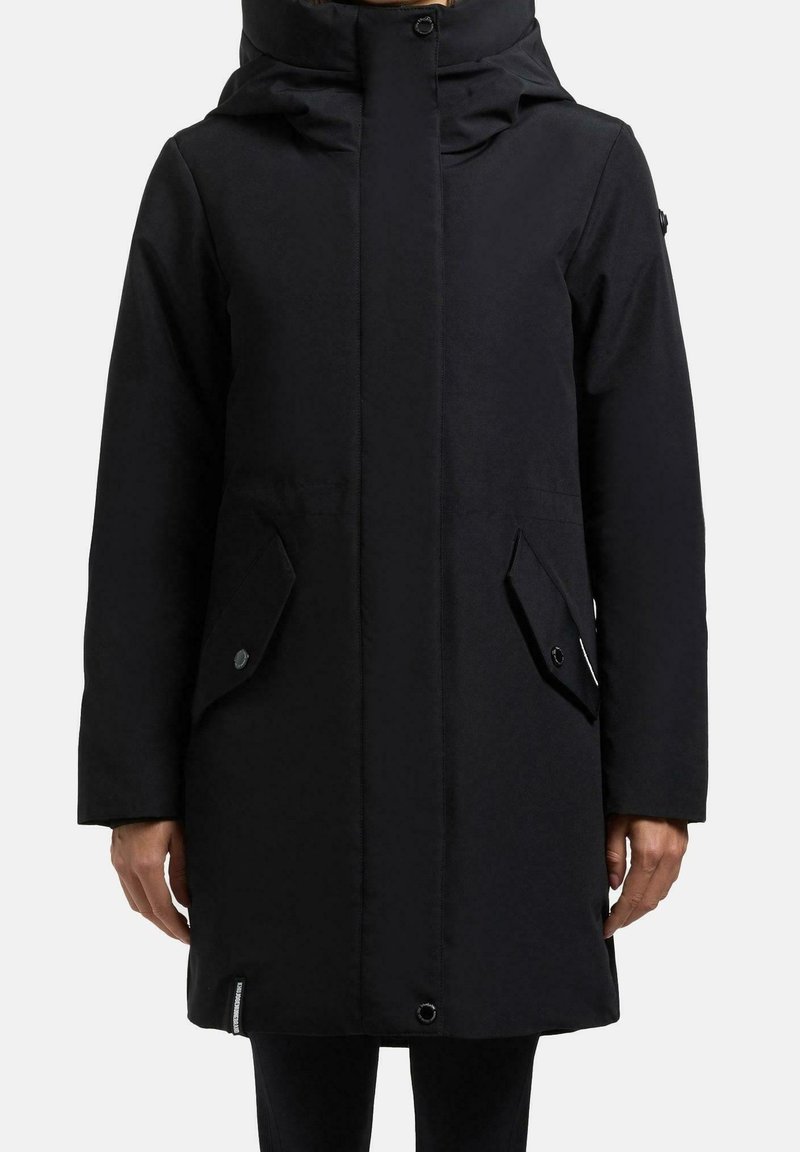 Manteau d'hiver long noir avec un col montant, une fermeture éclair frontale cachée et des poches à rabat à boutons-pression, présenté sur une personne devant un fond uni.