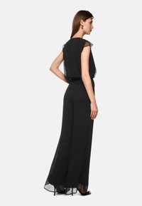 Schwarzer Jumpsuit mit einem fließenden, transparenten Oberteil und taillierter Taille. Verfügt über weit geschnittene Hosen und durchsichtige Akzente an den Ärmeln.