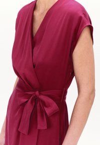 Vestido envolvente burdeos con mangas cortas y un cinturón atado en la cintura. La tela tiene una textura suave con un brillo sutil.