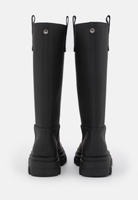 Zwarte rubberen kniehoge laarzen met stevige zolen, voorzien van stiksels en aantreklussen aan de zijkanten voor gemakkelijk aantrekken.