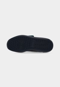 Black rubber shoe sole featuring a textured pattern with circular grips, flat design and slight curvature at the heel, made for stability.