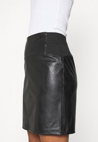 Schwarzer Leder-Minirock mit glatter Textur, elastischem Bund und seitlichen Taschen, tailliert geschnitten und in knielanger Länge.