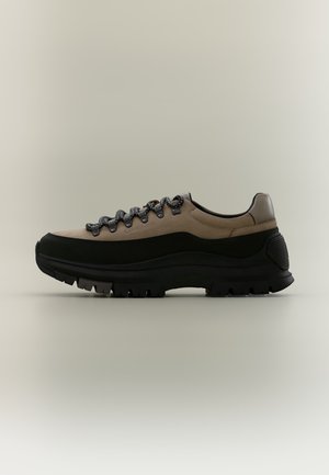 Chaussure de randonnée beige et noire avec une semelle épaisse et robuste, un bout rond et des lacets noirs et gris, vue de profil sur un fond neutre.