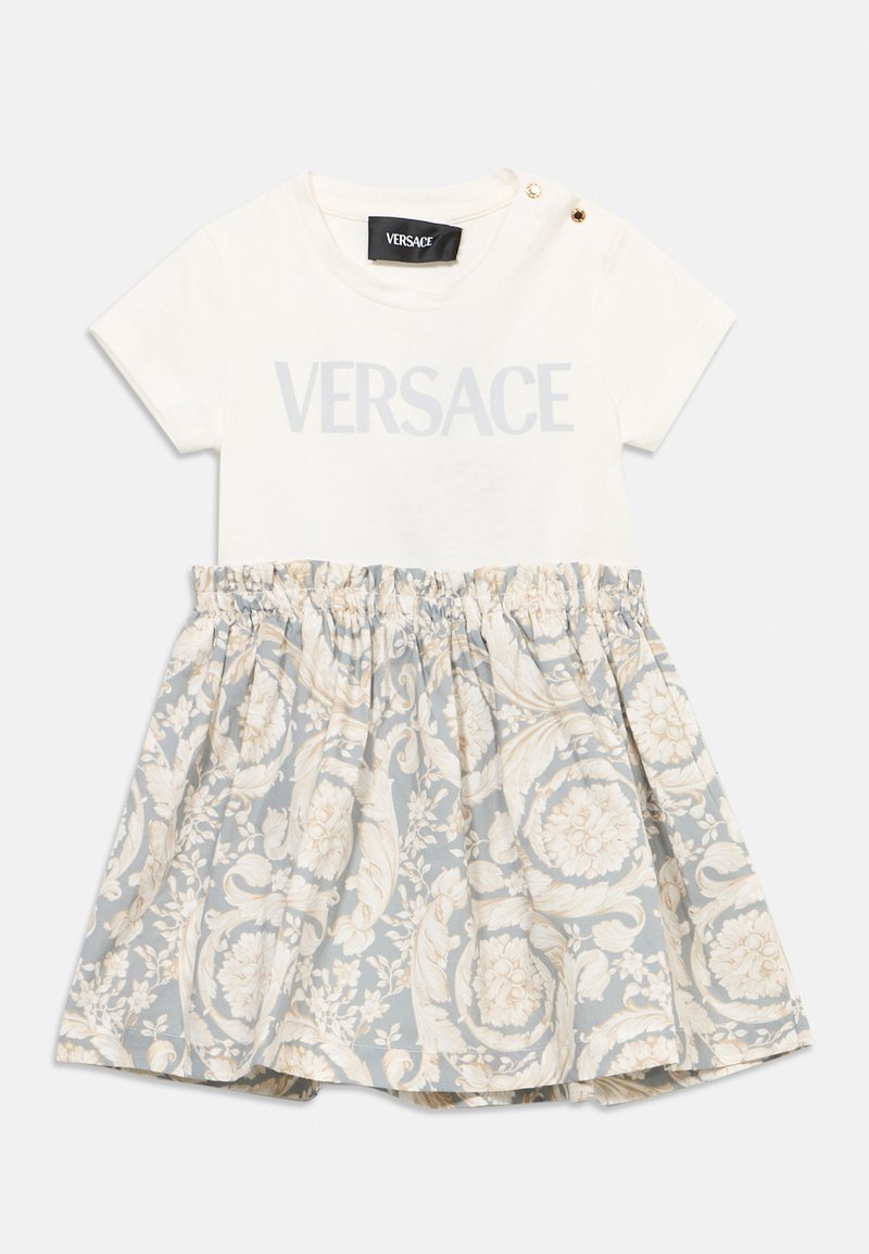 Λευκό φόρεμα για νήπιο με κοντά μανίκια, λεπτομέρειες με χρυσά κουμπιά στον ώμο, φούστα με γκρι και κρεμ λουλουδάτο σχέδιο και σούρες, λογότυπο Versace στο στήθος.