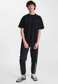 Črna bombažna majica s kratkimi rokavi in majhnim grafičnim motivom. Ujemajoče se s črnimi hlačami s sivimi poudarki in sivimi supergami z belimi vezalkami.