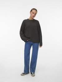 Maglione oversize marrone scuro con collo rotondo, abbinato a jeans a gamba larga blu chiaro e sneakers nere con dettagli beige.