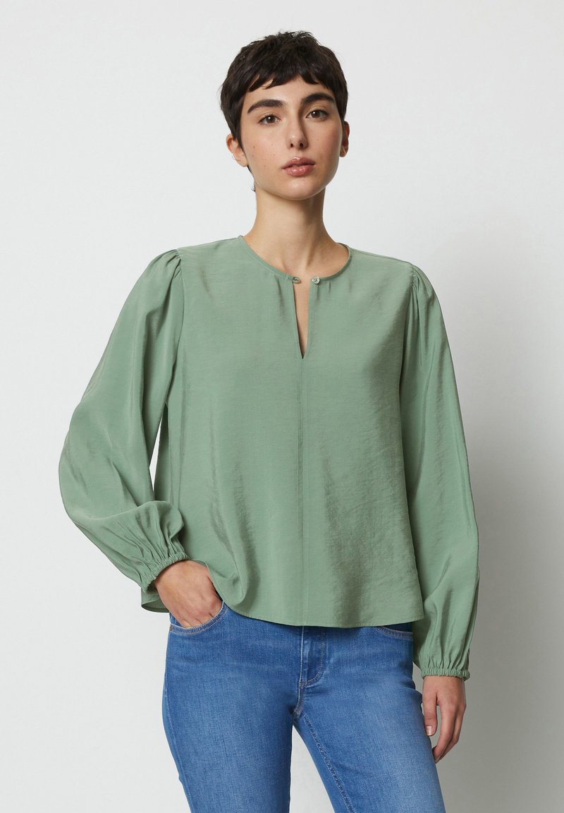 Blusa verde con una texture morbida e liscia, scollatura rotonda e dettaglio dei bottoni. Presenta maniche lunghe e arricciate e una vestibilità comoda.