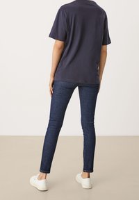 Camiseta de algodón azul marino de manga corta, combinada con jeans de mezclilla oscuros ajustados y zapatillas blancas; diseño liso sin patrones.