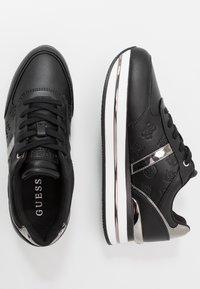 Czarne sneakersy z górną częścią ze skóry, dekoracyjnym wzorem logo, srebrnymi akcentami i białą podeszwą pośrodkową. Posiadają wyściełany kołnierz i zapięcie na sznurówki.