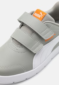 Baskets en cuir gris avec des accents blancs, deux bandes velcro et une languette en mesh gris. Présente le logo Puma en orange sur l'étiquette.