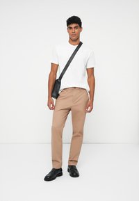 Pantaloni beige con un design su misura, abbinati a una maglietta bianca semplice e una borsa a tracolla nera; scarpe nere eleganti completano l'outfit.