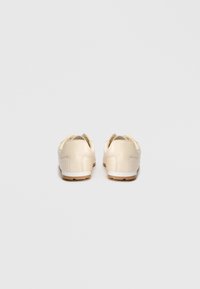 Baskets en cuir beige à la finition lisse, talon rond, design minimaliste et détails de couture subtils. Semelle extérieure en caoutchouc doux pour une meilleure traction.