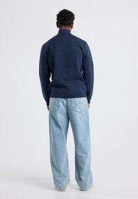 Navy fleece sweatshirt with a high collar, paired with light blue loose-fit jeans. Sweater has ribbed cuffs and hem.