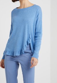 Pull bleu clair présentant une texture douce, une coupe décontractée, un large décolleté et un ourlet à volants. Associé à un pantalon bleu clair assorti.