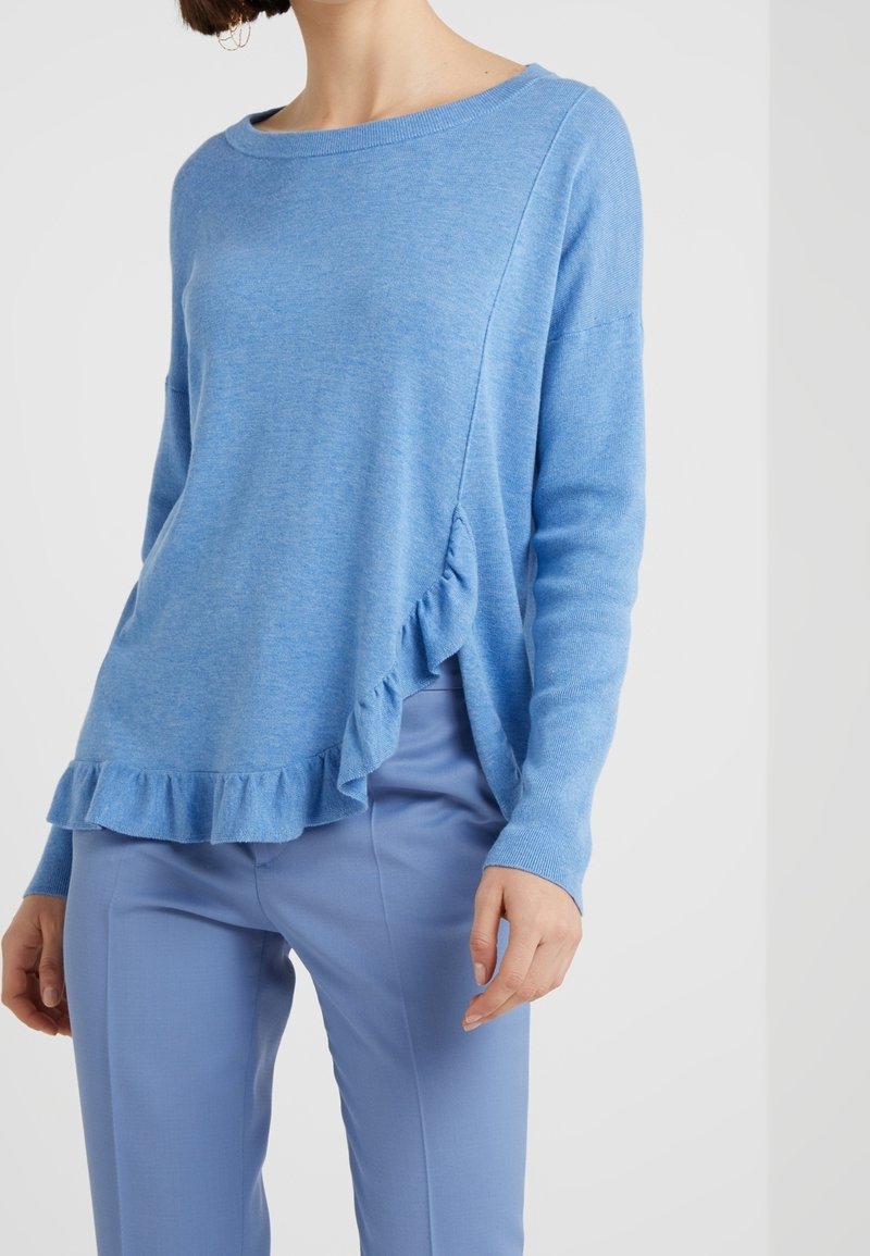 Pull bleu clair présentant une texture douce, une coupe décontractée, un large décolleté et un ourlet à volants. Associé à un pantalon bleu clair assorti.