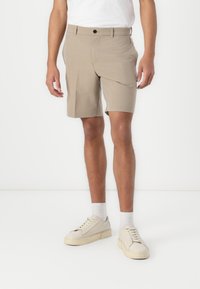 Beige shorts with a straight fit, side pockets, and a single button closure, paired with white sneakers and ankle-length socks.