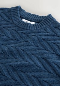 Ciemnoniebieski sweter dziergany z prążkowanym dekoltem i fakturowanym wzorem w jodełkę. Wykonany z miękkiej tkaniny, z detalicznym przeszyciem.