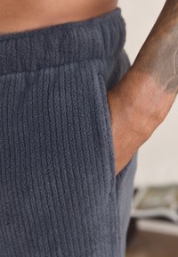 Dark grey corduroy joggers with a textured ribbed surface, featuring side pockets and an elastic waistband.