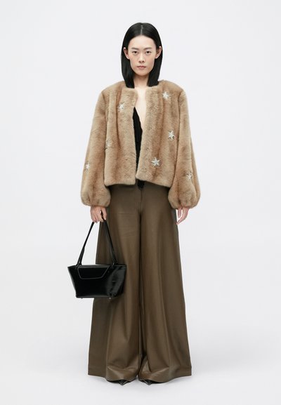 Brūns kažoks ar sudraba zvaigžņu rotājumiem, apvienots ar melnu topu, plašām brūnām biksēm un melnu rokassomu. Balts fons.